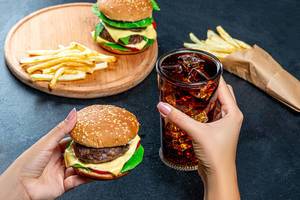 In one hand Burger, in the second the glass with cold Cola. The concept of unhealthy eating
