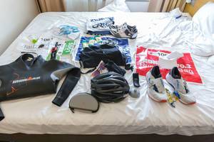 Ironman-Ausrüstung mit Neoprenanzug, Schwimmbrille, Fahrradhelm, Laufschuhen, Energie Snacks und der Wettkampf-Startnummer