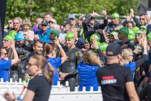 Ironman-Teilnehmer in Neoprenanzügen und Badekappen, werden im finnischen Lahti vor dem Schwimmwettkampf angefeuert
