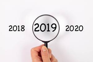Jahreszahl 2019 unter Lupe, daneben 2018 und 2020 auf weißem Hintergrund