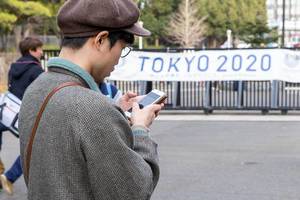Japanese looking at a smartphone with Tokyo2020 poster in the background