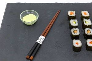 Japanische Essstäbchen mit Sushi und Wasabi auf schwarzer Schieferplatte