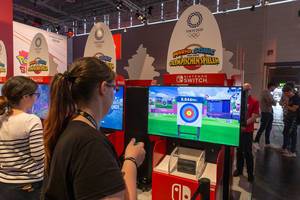 Junge Frau testet das virtuelle Bogenschießen im Videospiel Mario&Sonic bei den Olympischen Spielen, an der Nintendo Switch Spielstation