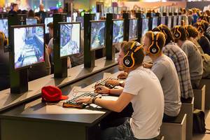 Junge Männer sitzen in einer Reihe und zocken ein Mehrspieler-Ego-Shooter Videospiel von Blizzard