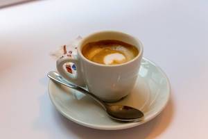 Kaffee mit schöner Crema mit Löffel und Zuckerbeutel auf Untertasse