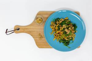 Kale Spätzle Noodles with mushrooms, walnuts and cream sauce on a blue plate, on a wooden chopping board and white background