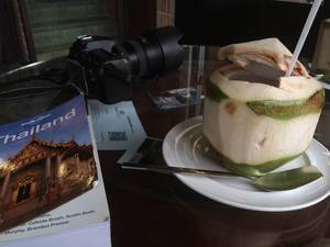 Kamera, Reiseführer Thailand und Getränk in einer Kokosnuss auf dem Tisch