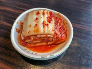 Kimchi mit Soße in weißer Schüssel auf Holztisch