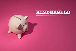 Kindergeld Aufschrift auf pinker Hintergrund, neben einem rosa Sparschwein