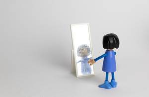 Kinderspielzeug: Kleine Puppe bestaunt ihre Reflektion in Miniatur-Standspiegel - Nahaufnahme
