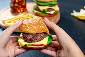 Klassischer Burger mit Rindfleischfrikadelle und Käse, in Frauenhänden