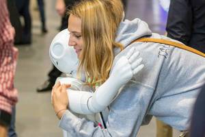 Kleiner humanoider Roboter Pepper von Humanizing Technologies interagiert mit Menschen und umarmt eine Frau auf der Bits & Pretzels Gründermesse
