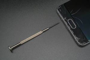 Kleiner Schraubenzieher und defektes Smartphone vor dunklem Hintergrund