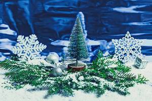 Kleiner Weihnachtsbaum zwischen beschneiten Tannenzweigen, Schneeflocken und Weihnachtsbaumkugeln