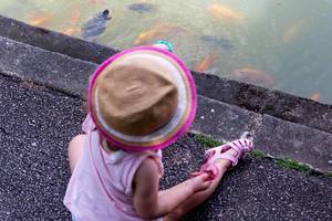Kleinkind mit Hut füttert Fische