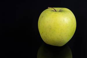 Knackiger grüner Apfel isoliert votrschwarzem Hintergrund mit diskreter Reflektion