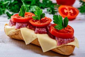 Knuspriges Sandwich-Baguette mit Käse, geräucherter Wurst, Tomaten und grünen Kräutern