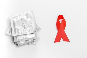 Kondome und rote Schleife vor einem weißen Hintergrund - das Konzept der Verhütung gegen beim Geschlechtsverkehr übertragenen Krankheiten