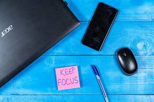 Konzentration bewahren: Notizzettel mit dem Text "Keep Focus", neben einem Computer, Maus und Handy im Homeoffice