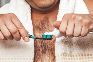 Konzept der Mundhygiene: Ein Mann mit Handtuch drückt Zahnpasta auf seine Zahnbürste