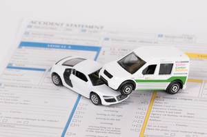 Konzept von Schadensmeldung nach Autounfall mit Spielzeugautos auf Versicherungsunterlagen