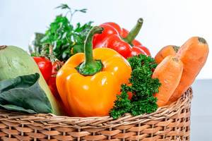 Konzeptbild Gesundes Essen: Farbenfrohes Gartengemüse wie Möhren, Paprika und Zucchini, mit frischen Kräutern in einem geflochtenen Korb