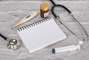 Konzeptbild mit Notizbuch, Medizin, Fieberthermometer, Spritze und Stethoskop