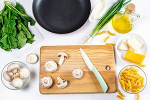 Konzeptbild zum Thema "Gesund kochen": Pastazubereitung mit Pilzen, Lauchzwiebeln, Spinat, Öl, Käse und Nudeln