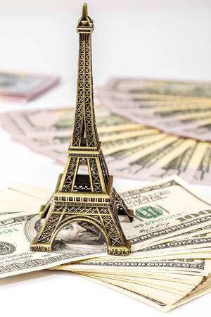 Konzeptbild zum Thema Reiseplanung zeigt einen Eiffelturm auf einem Geldstapel mit Dollarscheinen