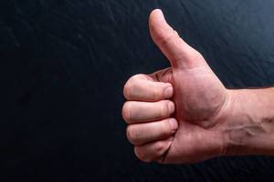 Konzeptbild zur positiven Zustimmen zeigt eine Männerhand vor schwarzem Hintergrund mit dem Daumen nach oben, als ein "Gefällt mir" Symbol