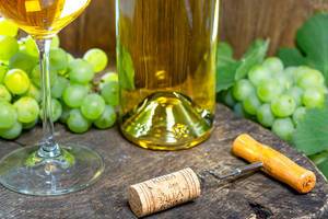 Korkenzieher mit Holzgriff vor einer Weinflasche und grünen Weintrauben