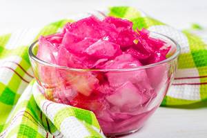 Krautsalat eingelegt in pinker Marinade in Glasschüssel vor grün-weißem Küchentuch