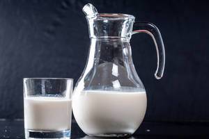 Krug und Glas mit frischer Milch vor dunklem Hintergrund
