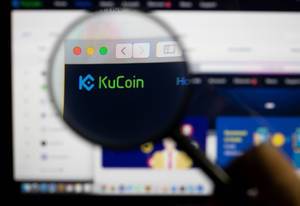 KuCoin logo on a computer screen with a magnifying glass