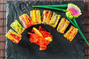 Kunstvoll angerichtetes, farbiges Sushi mit Wasabi, Lachs und Zitrone auf Steinplatte