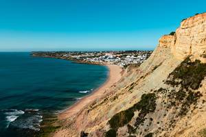 Küste mit steilen Klippen und weißem Dorf im Hintergrund bei Reserva da Luz, Portugal