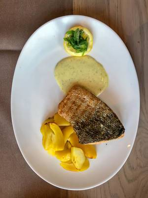 Lachsfilet-Fisch vom Grill mit Kartoffeln und Kräuterdressing neben einer Zitrone auf einem weißen ovalen Teller
