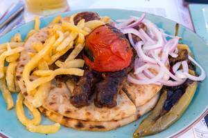 Leckere Kebab Pita mit Tomaten aus Paros, Zwiebeln und gegrillter griechischer Paprika auf blauem Teller