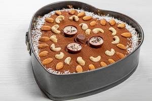 Leckerer, hausgemachter Schokoladen Kuchen in Herzform mit Nüssen auf weißem Holzhintergrund