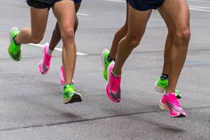 Legs of marathon runners wearing Nike ZoomX Vaporfly Next% running shoes in the pink and green versions