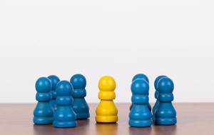 Leiter / Führungskraft als gelbe Spielfigur dargestellt, umgeben von blauen Bauern-Spielsteinen als Mitarbeiter