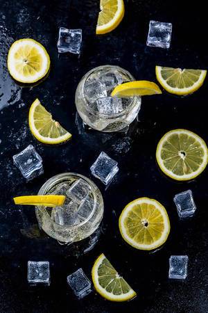 Lemonade with ice cubes and sliced lemon on black background. Top view