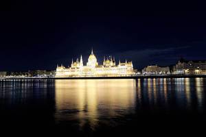 Leuchtendes Parlamentsgebäude bei Nacht in Budapest, Ungarn, mit Wasserreflexion auf der Donau