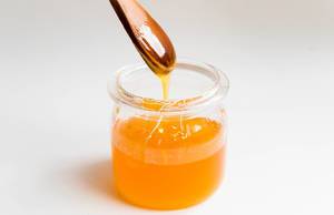 Liquid orange honey dropping from a wooden spoon