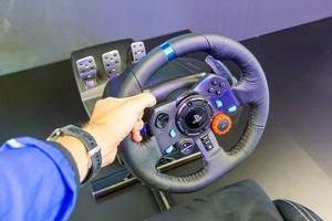 Logitech G29 Driving Force - Mann hält das Leder-Rennlenkrad mit Pedale-Set für PlayStation und PC