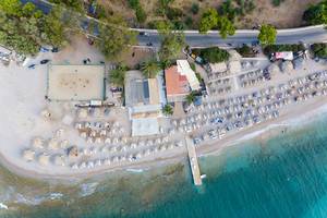 Luftbild des griechischen Καiκι-Strands, mit Bastsonnenschirmen und Touristen auf Strandliegen, an der Küste von Spetses