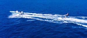 Luftbild eines stehenden Wasserskifahrers hinter einem Sportboot auf dem Agogischen Golf