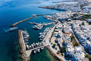 Luftbild von weißen Kalksteinhäusern am Küstenabschnitt und  Segelboote im Hafen im Mittelmeer, vor Naoussa in Griechenland