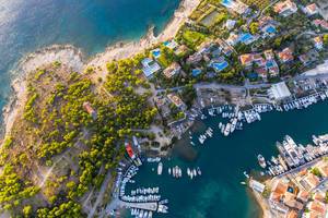 Luftbild von Wohnhäusern und Hotels mit Pool an der Hafenbucht von Kouzounos, südöstlich von Spetses, Griechenland