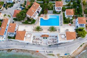 Luftbild zeigt das Hotel Nissia mit Ferienwohnungen und Palmen am eigenen Pool, an der Küste von Spetses